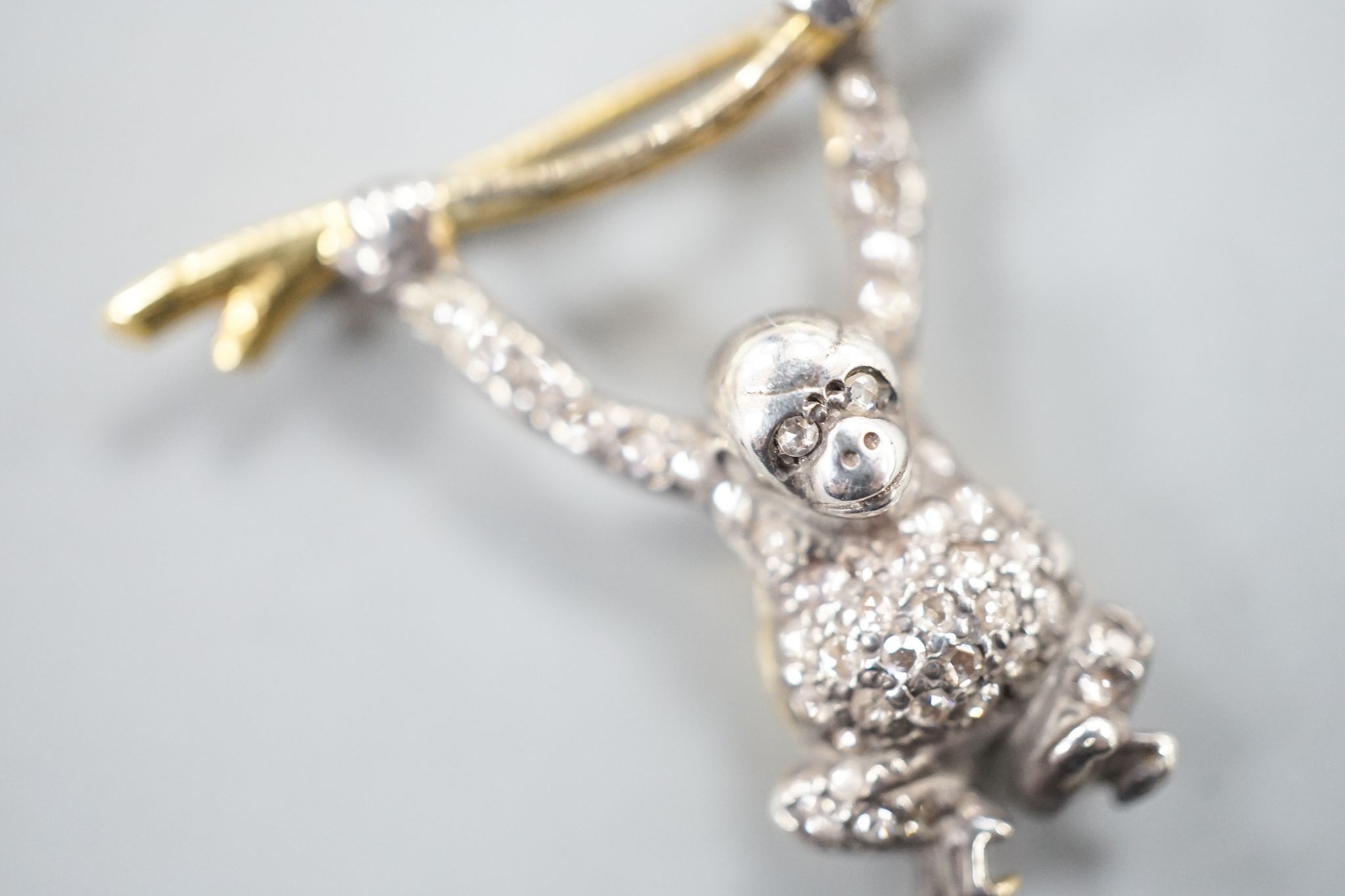 A Victorian style novelty white and yellow metal, diamond chip set brooch, modelled as a monkey hanging from a branch, 26mm drop, width 30mm.